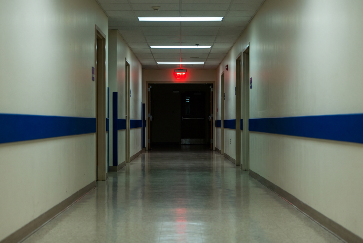 Couloir d'hôpital désert la nuit, murs crème et lumière rouge au fond