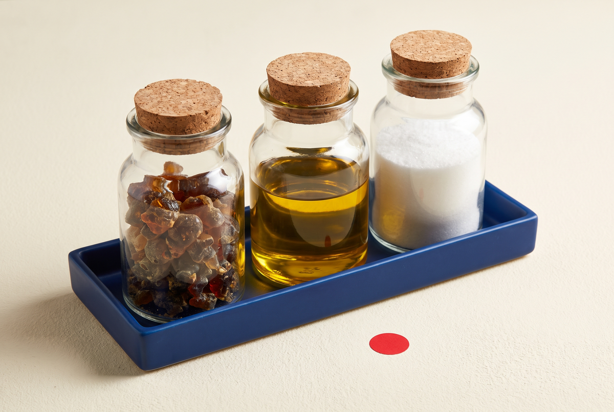 Trois récipients de verre contenant résine, huile et poudre cristalline sur un plateau bleu